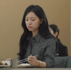 a woman sitting at a table with chopsticks in her hand and looking down