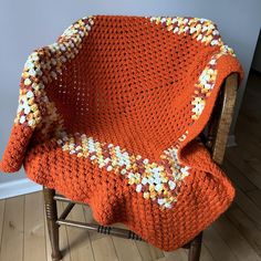 an orange crocheted blanket sitting on top of a wooden chair