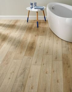 a bath tub sitting next to a wooden floor in a bathroom with white walls and wood floors