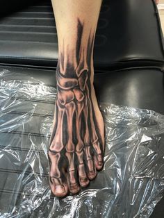 a person's foot with a skeleton tattoo on it and one hand resting on the ground