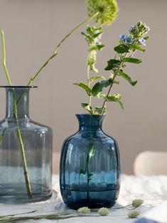 two blue vases with flowers in them on a white table cloth and one is empty