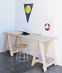 a wooden desk sitting in front of a white wall next to a chair and stool