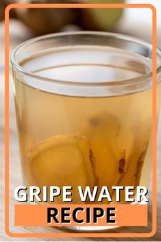 a glass cup filled with liquid sitting on top of a wooden table next to an apple