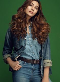 a woman with long red hair and jeans on posing for a magazine cover photo in front of a green background