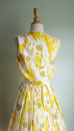 Now that's a cocktail dress! 🍸🍋 This vintage dress looks like an olive martini with a citrus twist, with its fun abstract dot and stem print, bursting with pops of orange, yellow and green on a cream background. It features a blouson-style bodice that buttons in the back; a cinched waist accented by a matching tie sash; and a full, twirly pleated skirt. (Pictured with a crinoline- not included - to demonstrate fullness; its white edge peeks out at the hem.) Bodice is lined; back metal zip at w Sleeveless Summer Cocktail Vintage Dress, 1950s Style Summer Cocktail Dress, Summer Dresses With Box Pleat And Full Skirt, Retro Pleated Summer Dresses, Mid-century Summer Party Dresses, 1950s Style Sleeveless Green Dress, 1950s Style Yellow Dress For Garden Party, Green Summer Dresses In Vintage Style, Green Summer Dresses For Vintage Fashion