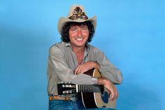 a man wearing a cowboy hat and holding a guitar in front of a blue background