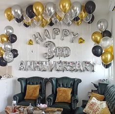 a living room filled with black couches and gold and silver balloons hanging from the ceiling