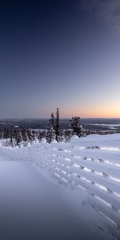 the sun is setting over some snow covered hills and trees in the foreground, with an expanse of deep blue sky above