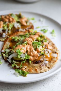 two tacos on a white plate topped with lettuce and sauce