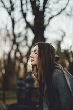 a woman sitting on the ground with her eyes closed and long hair blowing in the wind