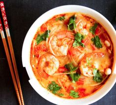 a bowl of shrimp soup with chopsticks next to it on a black surface