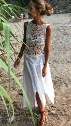 a woman standing on top of a sandy beach next to tall grass and palm trees