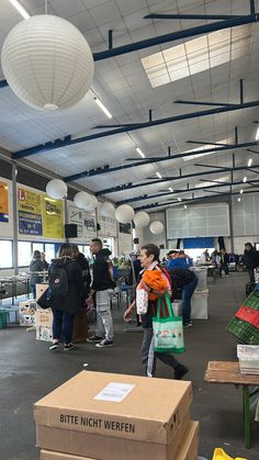 people are shopping in an open building with boxes on the floor and lights hanging from the ceiling