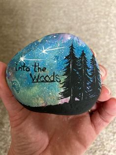 a hand holding a painted rock that says into the woods