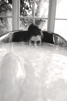 a woman in a bathtub with her head above the water looking at the camera