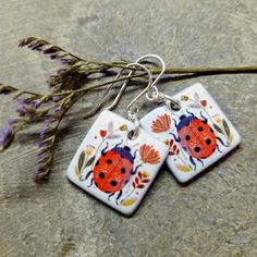 These earrings are so pretty!  Bright folkart ladybird and flowers decorate these handmade ceramic earrings.  Handmade using blue earthenware clay, glazed both sides and kiln-fired three times.  They measure 1.8 x 1.8 cm and hang from excellent quality, sturdy, sterling silver earring wires.  They are presented in an attractive grey jewellery box making them an ideal gift. Red Nature-inspired Earrings For Gift, Artsy Enamel Earrings As Gift, Nickel-free Enamel Flower Earrings Gift, Whimsical Nickel-free Flower Earrings As Gift, Whimsical Nickel-free Flower Earrings For Gifts, Gift Nickel-free Enamel Flower Earrings, Handmade Enamel Drop Flower Earrings, Hand Painted Dangle Flower Earrings For Gift, Cute Handmade Enamel Earrings