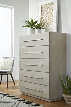 a white dresser sitting on top of a hard wood floor next to a chair and potted plant