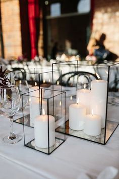 candles are placed in glass containers on a table with white linens and place settings