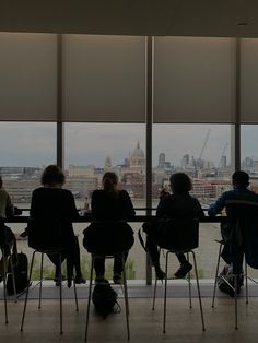 four people sitting at a table in front of large windows with cityscape behind them