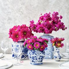 purple flowers in blue and white vases sitting on a table with wine glasses, plates and utensils