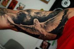 a man's arm with a dove tattoo on it and clouds in the background