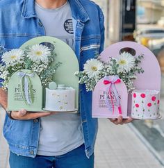 a man is holding two flower vases with daisies in them and one has a gift box