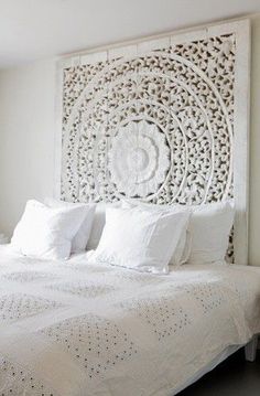 a bed with white sheets and pillows in a bedroom next to a wall hanging on the wall