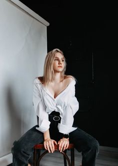 a woman sitting on top of a wooden chair in front of a white wall and black background