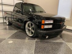 a black truck parked in a garage next to a white wall and floor with a checkerboard pattern on the floor