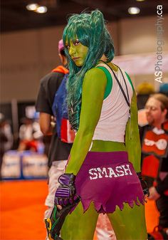 a woman dressed in green and purple is standing with her hands on her hips while wearing gloves