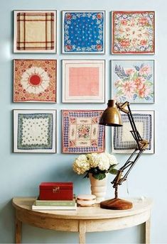 a table with a lamp and some pictures on the wall above it, along with flowers