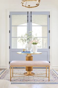 a dining room table and bench in front of a blue door with two vases on it