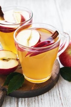 two glasses filled with apple cider on top of a wooden board