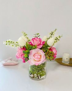 a vase filled with pink and white flowers sitting on top of a table next to a candle