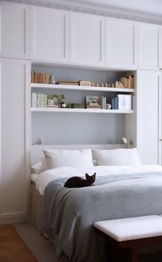 a cat laying on top of a bed next to a white book shelf filled with books