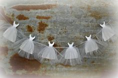 three white tulle dresses hanging on a line against a rusted metal wall with peeling paint