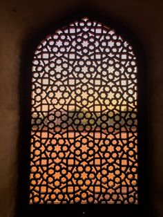 an ornate window in the middle of a building with a view of a field through it