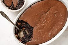 two bowls filled with brownie pudding on top of a white counter next to a spoon