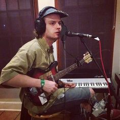 a man sitting in front of a microphone while holding a guitar and wearing headphones