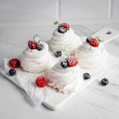 three meringue cupcakes with berries and powdered sugar