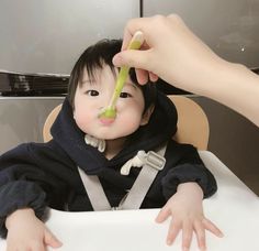 a baby sitting in a high chair being fed with a spoon by someone's hand