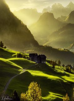 the sun shines brightly on green hills and houses in the distance with mountains in the background