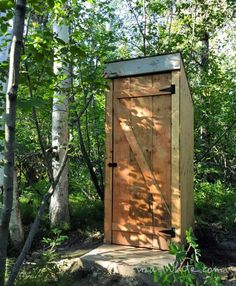 a wooden outhouse in the woods surrounded by trees and bushes with its door open