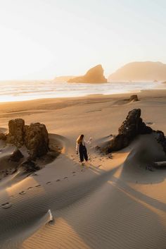 a person standing on top of a sandy beach next to the ocean with rocks in the sand