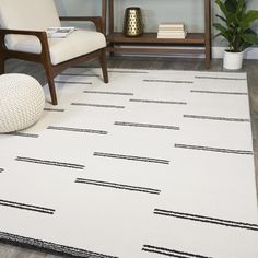 a white rug with black lines on it in front of a chair and bookshelf