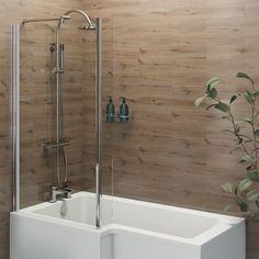 a white bath tub sitting next to a plant in a room with wood wallpaper