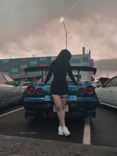 a woman sitting on the back of a blue car in a parking lot next to other cars