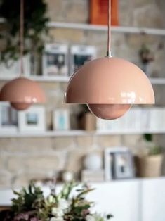 two pink lamps hanging from the ceiling above a dining room table with flowers on it