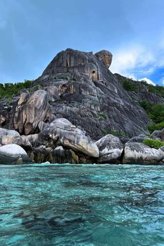 the water is crystal blue and there are rocks in front of it that look like they have faces on them