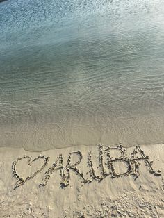 the word aruba written in sand at the beach with water and sky behind it